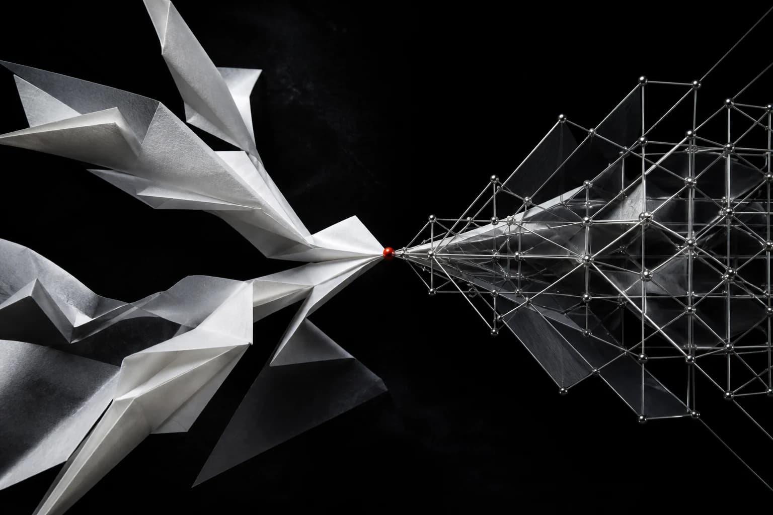A field of folded white forms and a precise silver lattice meet at one small red point against a deep black background